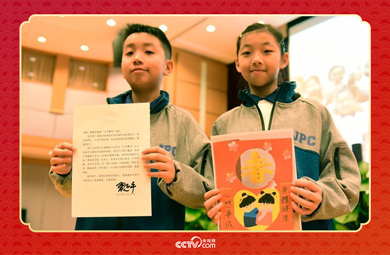 圖為香港“少年警訊”成員郭宏晞（左）展示習(xí)主席回信、羅顥凝（右）展示送給習(xí)主席的賀卡并合影。